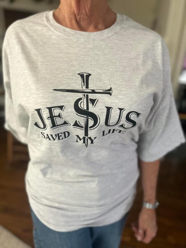 Light gray t-shirt with text: "Jesus Saved My Life" featuring a center cross out of nails. Available sizes: S-L Women's Cut