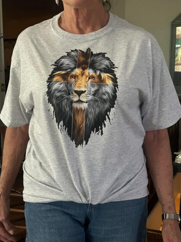 Light gray t-shirt featuring a realistic lion graphic in grayscale with a cross overlay. Available sizes: S-L Women's Cut